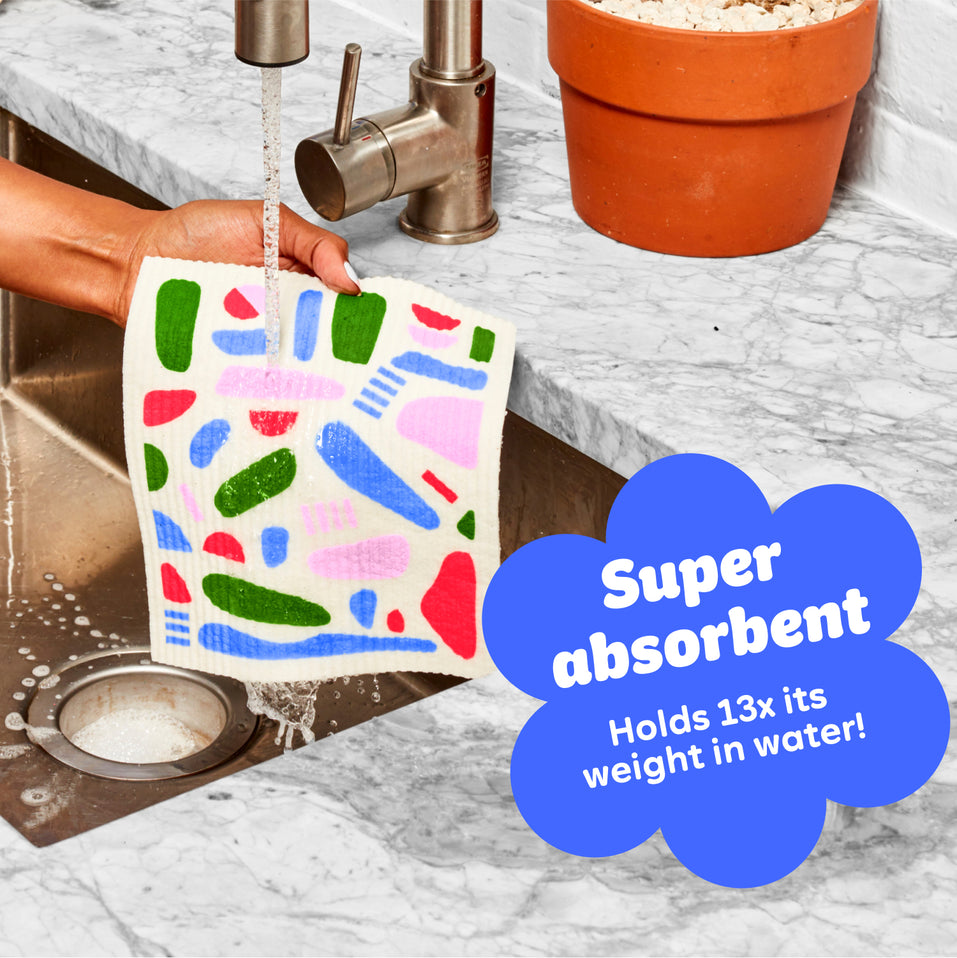 A super absorbent Who Gives A Crap durable Dream Cloth being washed under running water in a kitchen sink, showing how it can hold up to 13 times it’s weight in water.