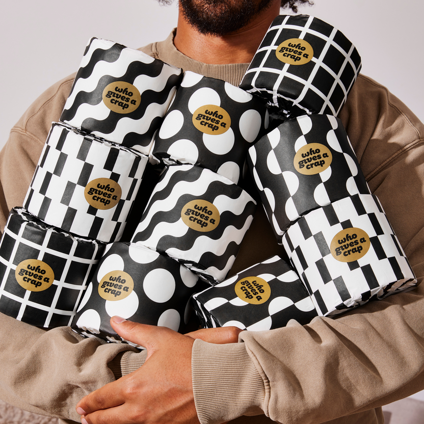 Man holds armful of patterned Who Gives a Crap bamboo toilet paper rolls