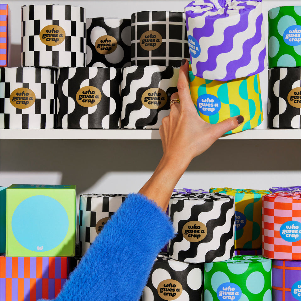 Hand reaching to shelf with colourfully wrapped eco-friendly toilet paper and tissue boxes.