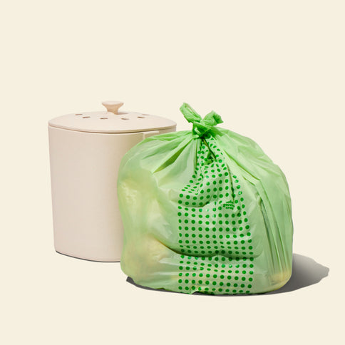 A full compostable food scrap bag with a patterned design is placed next to a closed kitchen food scrap bin.