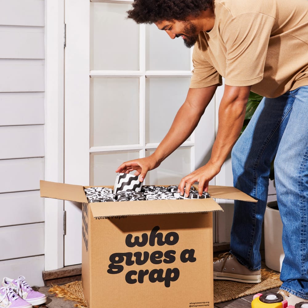 Man unboxes a box of 48 Premium toilet paper rolls.