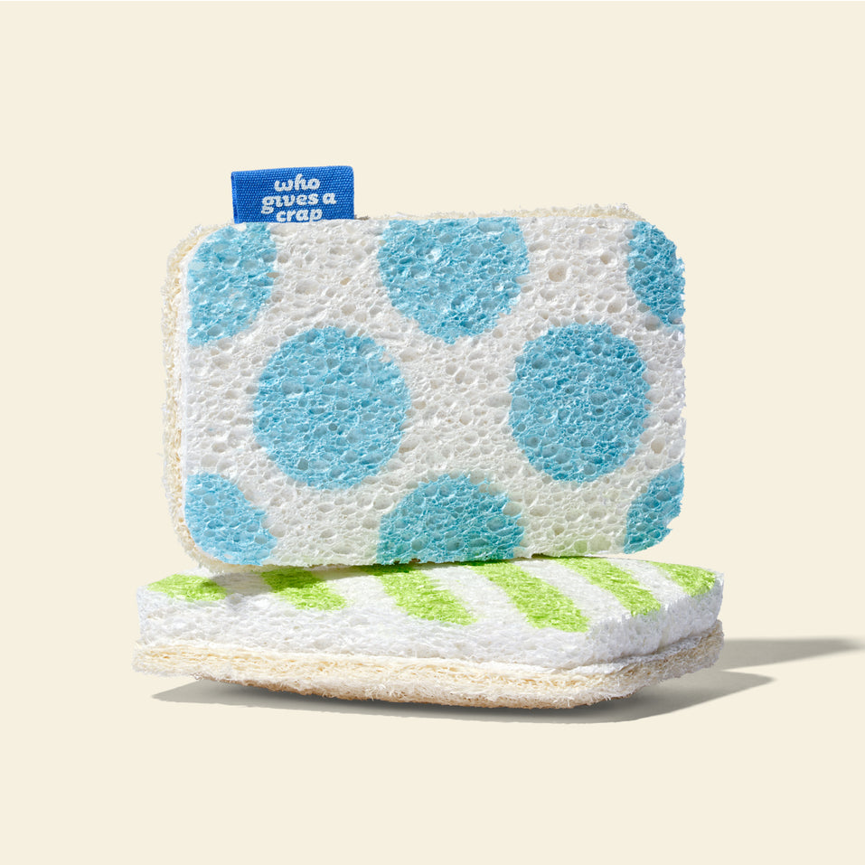 A Who Gives A Crap blue polka dot scrub sponge stacked on top of a green striped scrub sponge, showing the soft sponge side and natural loofah scrubbing side