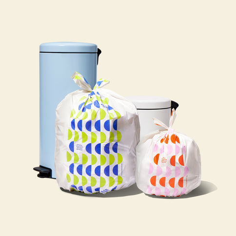 Two full garbage bags with patterned designs, displayed next to trash cans of varying sizes, highlighting the different bag sizes.