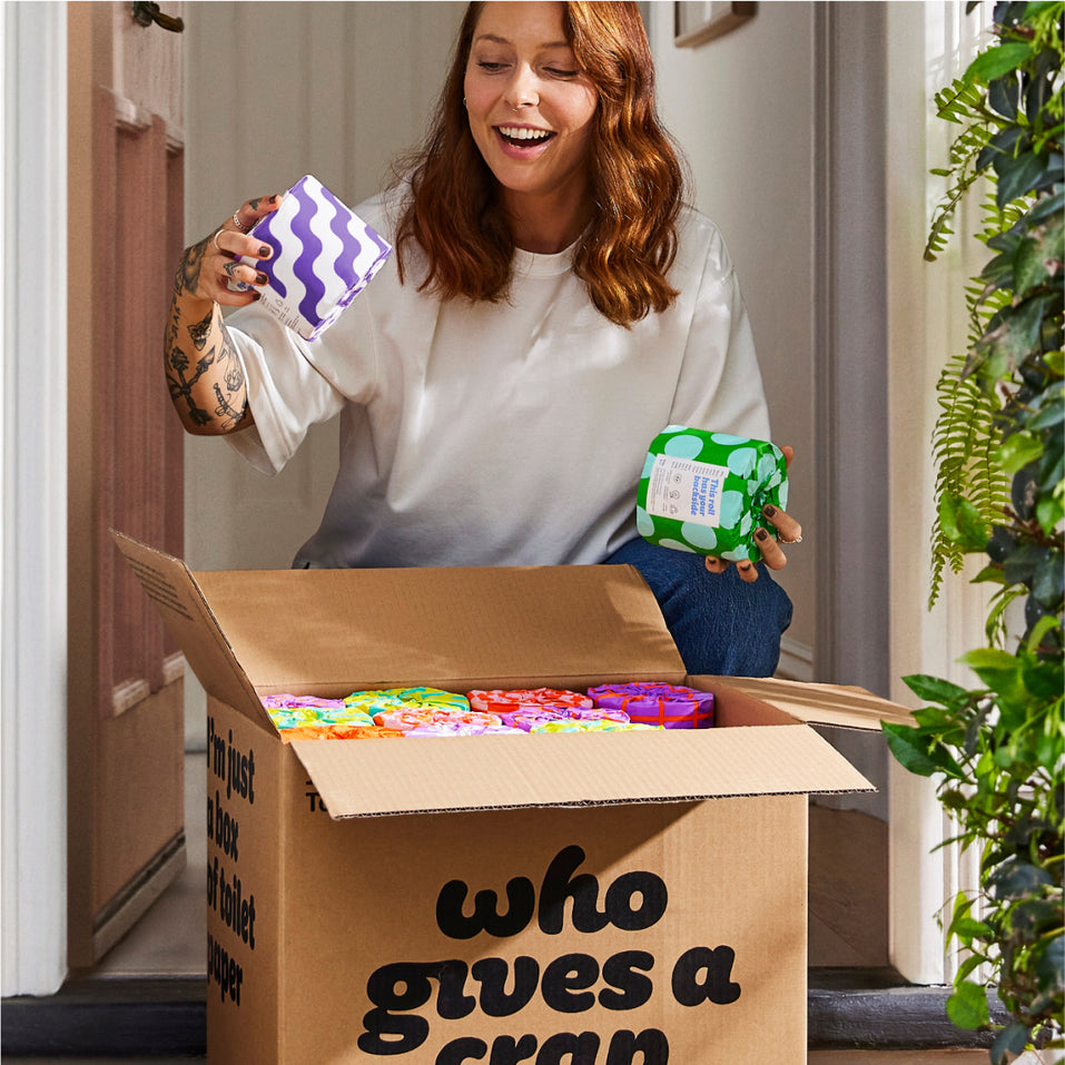 Woman collecting box of Who Gives a Crap toilet paper from front porch of home smiles as she opens box