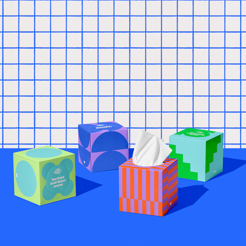 Four boxes of of Who Gives a Crap recycled tissues against blue and white bathroom wall.