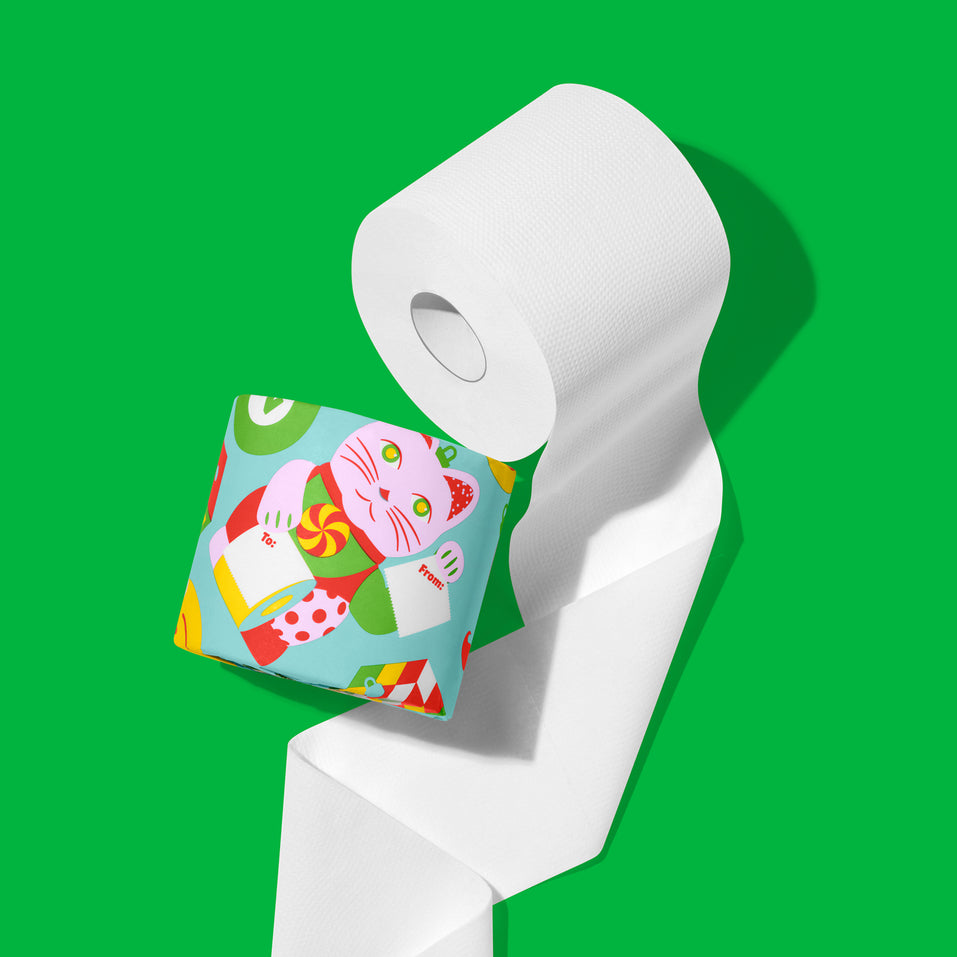 Close-up of an unrolled white roll of 3-ply bamboo toilet paper beside a roll in a festive wrapper, on a green background.