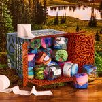 An open shipping box packed with park-design rolls sitting by a mountain lake in a forest.
