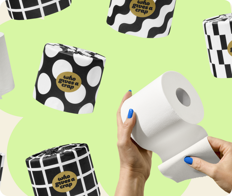 Hands with blue nail polish hold an unwrapped toilet roll, surrounded by rolls in black and white patterned wrappers.