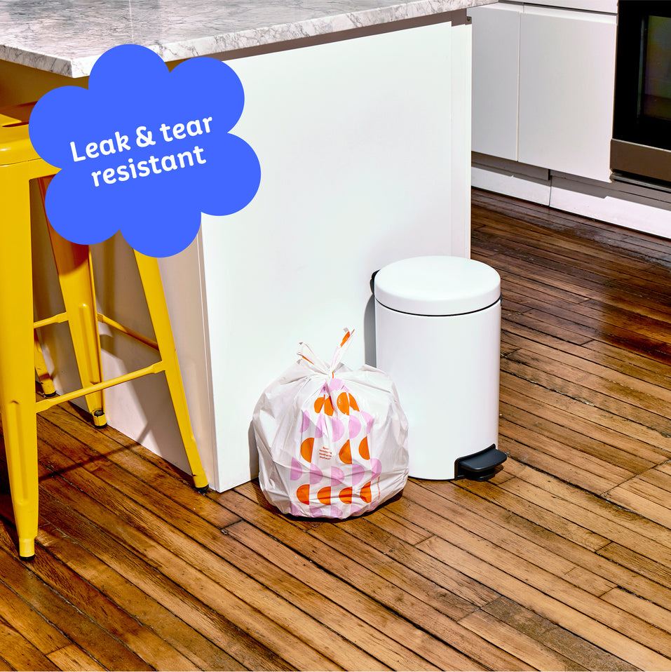 Who Gives a Crap small recycled trash bag sits full next to kitchen bin. Caption in corner reads ‘Leak & tear resistant’.