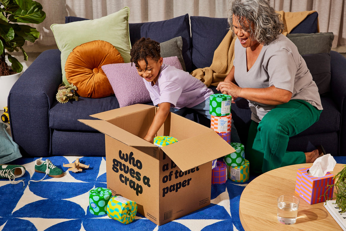 A grandmother and grandchild unboxing Who Gives A Crap rolls in the living room